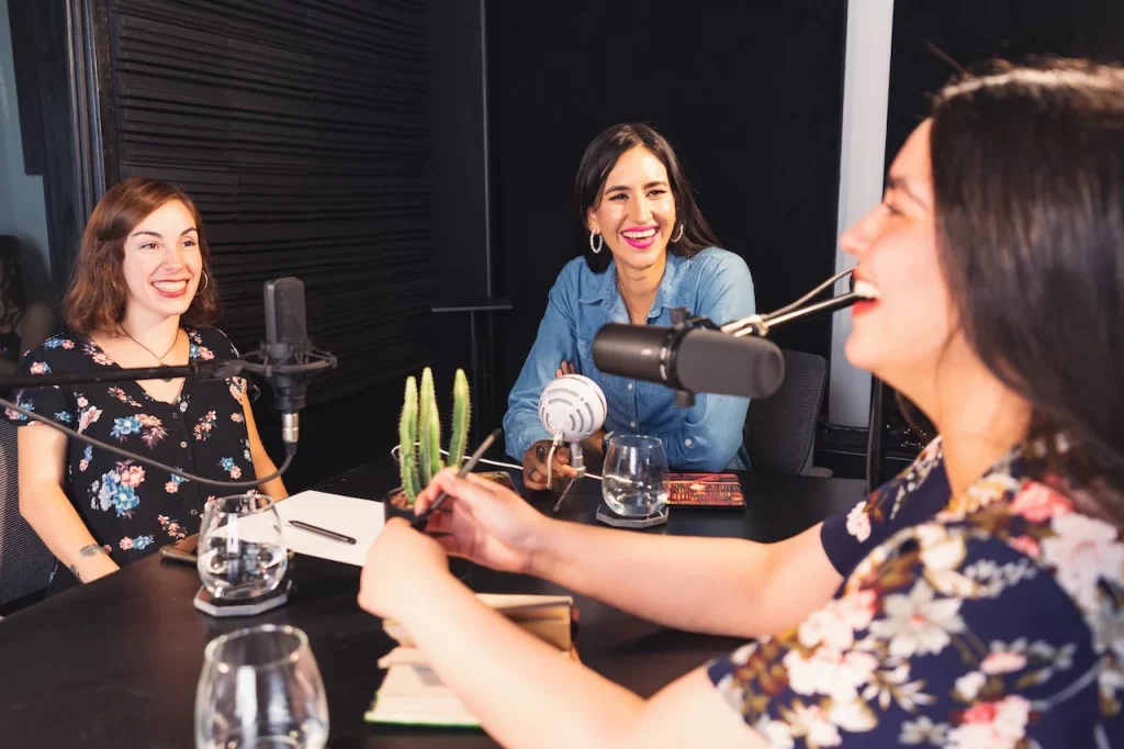 Three women hosting a panel podcast sitting down and using microphones